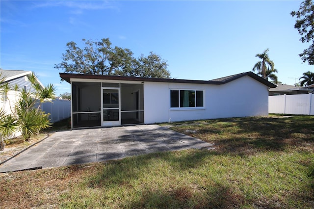 back of property with a sunroom, a patio area, and a lawn