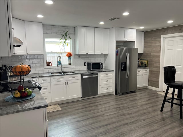 kitchen with appliances with stainless steel finishes, white cabinetry, dark wood-type flooring, sink, and extractor fan