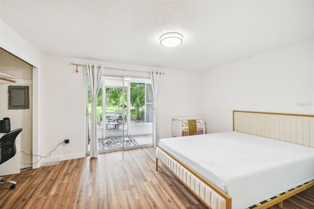 bedroom featuring light wood-type flooring, a textured ceiling, electric panel, and access to exterior