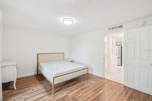 bedroom featuring a textured ceiling, stainless steel refrigerator, and light hardwood / wood-style floors