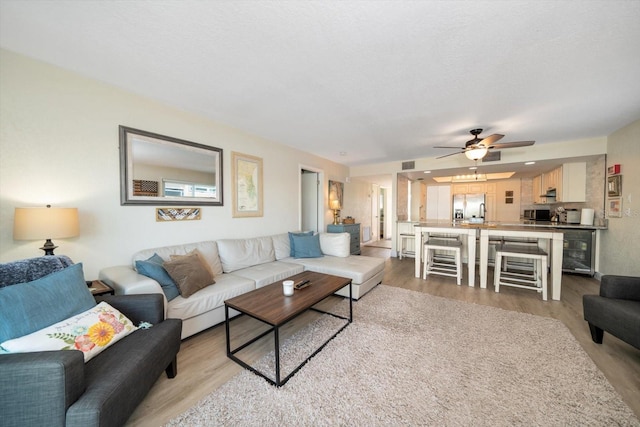 living room featuring light wood-type flooring, ceiling fan, and wine cooler