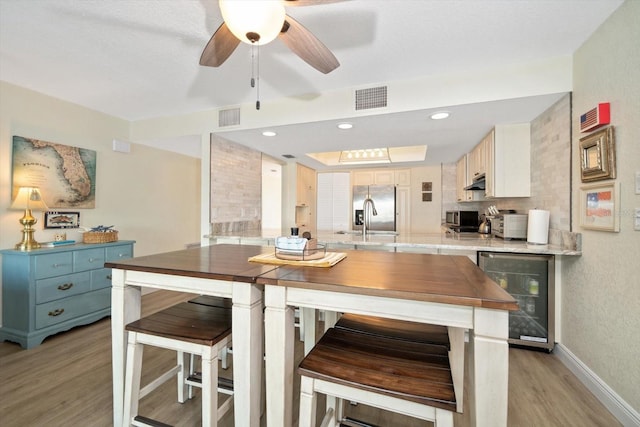 kitchen featuring light hardwood / wood-style floors, wine cooler, a breakfast bar area, ceiling fan, and sink