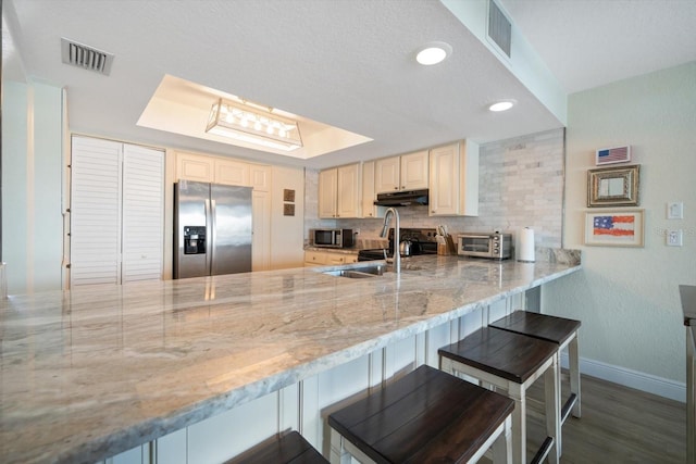 kitchen with light stone countertops, appliances with stainless steel finishes, dark hardwood / wood-style floors, and kitchen peninsula