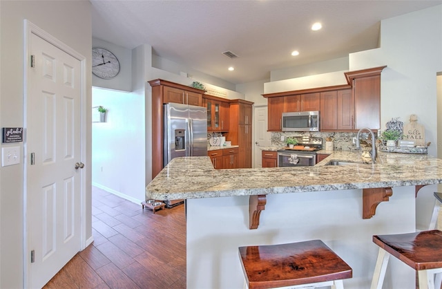 kitchen with sink, kitchen peninsula, stainless steel appliances, dark hardwood / wood-style floors, and a breakfast bar