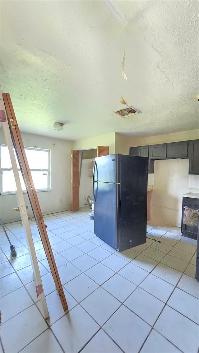 kitchen featuring black refrigerator, light tile patterned flooring, and a textured ceiling