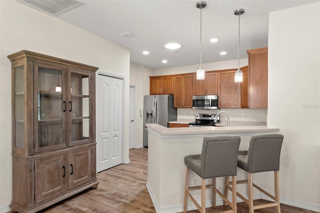 kitchen with a breakfast bar area, kitchen peninsula, light hardwood / wood-style flooring, stainless steel appliances, and decorative light fixtures