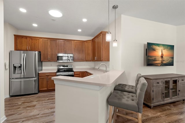 kitchen with pendant lighting, sink, kitchen peninsula, light hardwood / wood-style flooring, and appliances with stainless steel finishes