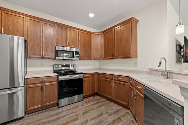 kitchen featuring light hardwood / wood-style floors, a textured ceiling, sink, stainless steel appliances, and decorative light fixtures