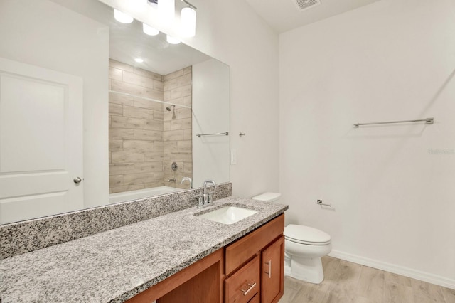 full bathroom featuring hardwood / wood-style floors, tiled shower / bath, vanity, and toilet