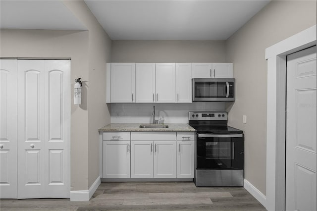 kitchen featuring decorative backsplash, appliances with stainless steel finishes, sink, light hardwood / wood-style flooring, and white cabinetry