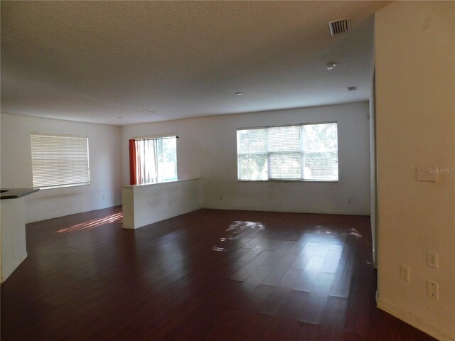 unfurnished room with a wealth of natural light, a textured ceiling, and dark hardwood / wood-style floors