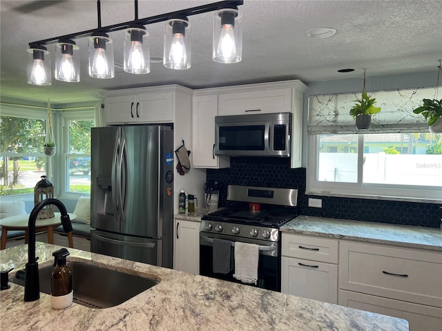 kitchen featuring a wealth of natural light, sink, stainless steel appliances, and white cabinets