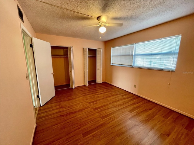 unfurnished bedroom featuring hardwood / wood-style floors, a textured ceiling, ceiling fan, and multiple closets