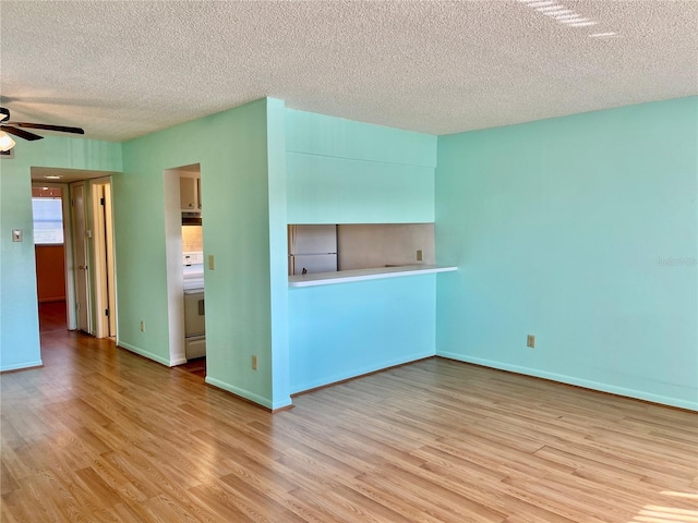 empty room with ceiling fan, light wood-type flooring, and a textured ceiling