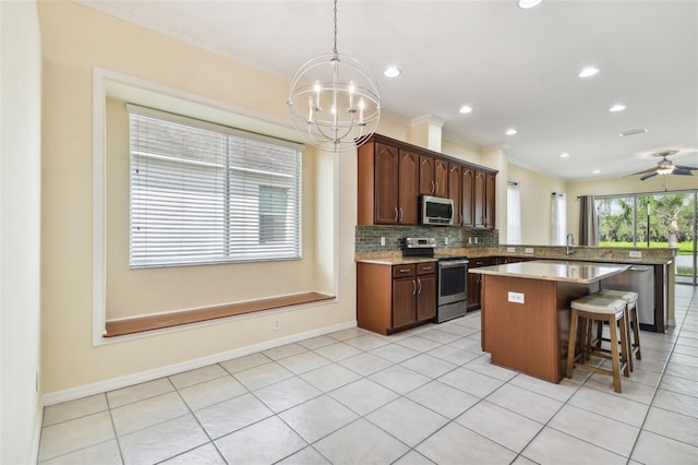 kitchen with a center island, ceiling fan with notable chandelier, hanging light fixtures, appliances with stainless steel finishes, and tasteful backsplash