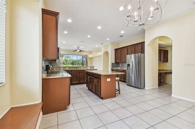 kitchen with a breakfast bar, ceiling fan with notable chandelier, hanging light fixtures, a kitchen island, and stainless steel fridge with ice dispenser