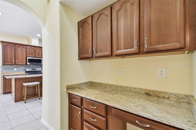 kitchen with light stone countertops, light tile patterned floors, backsplash, and stainless steel appliances