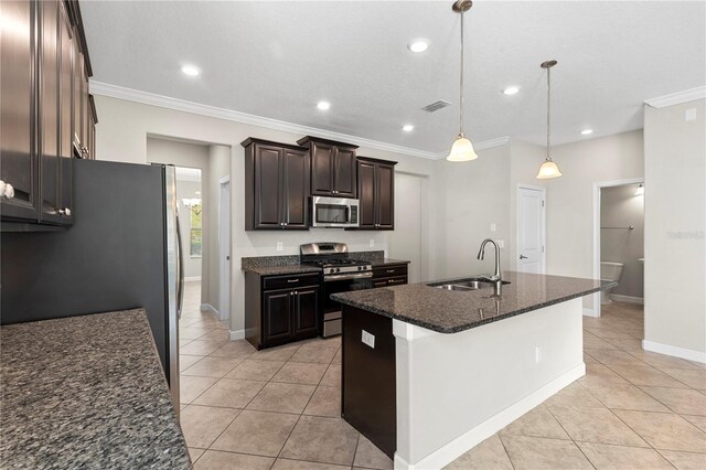 kitchen with decorative light fixtures, stainless steel appliances, dark stone counters, sink, and a center island with sink