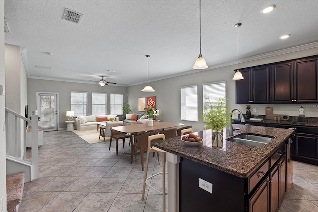 kitchen with crown molding, sink, dark brown cabinets, and a kitchen island with sink