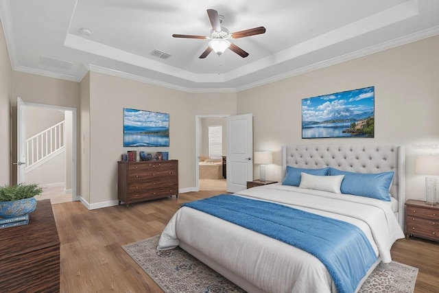 bedroom with ensuite bath, ceiling fan, light wood-type flooring, and a tray ceiling