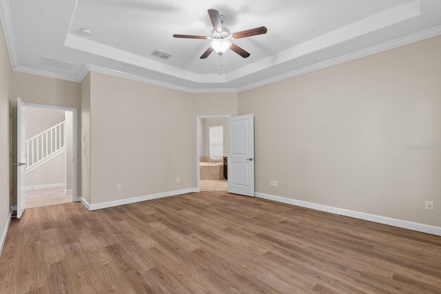 empty room with ceiling fan, a tray ceiling, ornamental molding, and light wood-type flooring