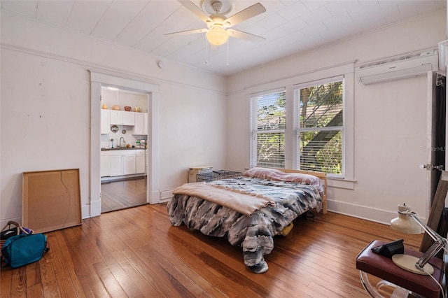 bedroom featuring wood-type flooring, a wall unit AC, ceiling fan, and sink