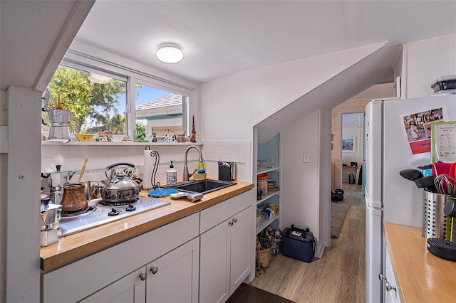 kitchen featuring decorative backsplash, white cabinetry, butcher block countertops, light hardwood / wood-style flooring, and sink