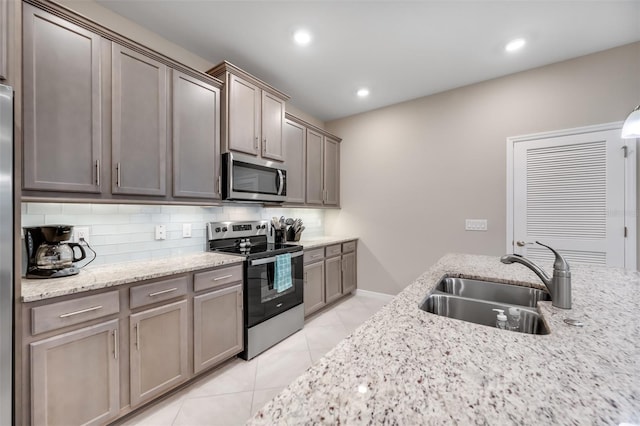 kitchen featuring appliances with stainless steel finishes, decorative backsplash, sink, and light stone countertops