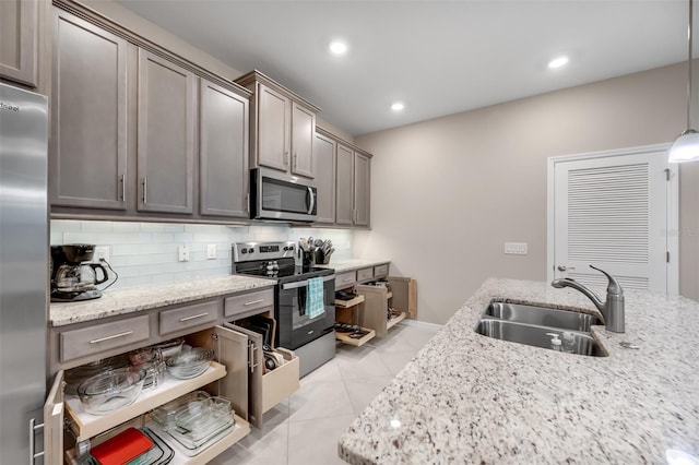 kitchen with light stone counters, hanging light fixtures, sink, stainless steel appliances, and decorative backsplash