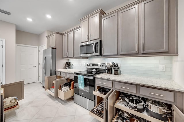 kitchen with backsplash, appliances with stainless steel finishes, light stone counters, and light tile patterned floors