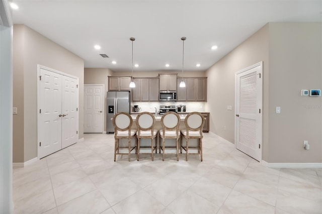 kitchen featuring decorative light fixtures, a center island with sink, stainless steel appliances, a kitchen breakfast bar, and decorative backsplash