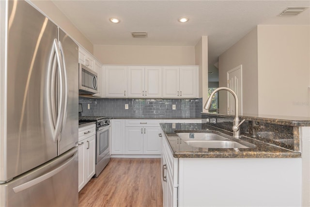 kitchen featuring stainless steel appliances, white cabinetry, dark stone counters, and sink