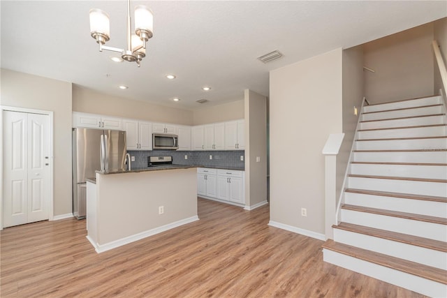 kitchen featuring a kitchen island with sink, white cabinets, decorative light fixtures, and appliances with stainless steel finishes