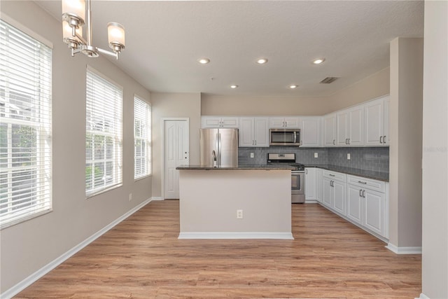 kitchen featuring white cabinets, appliances with stainless steel finishes, light hardwood / wood-style flooring, and hanging light fixtures