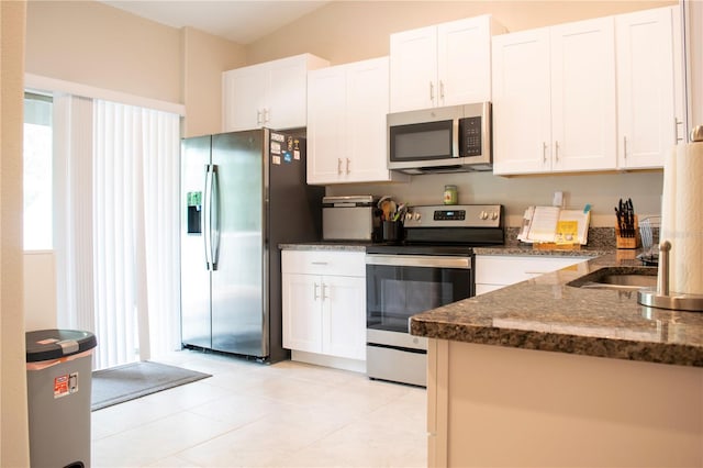 kitchen featuring appliances with stainless steel finishes, dark stone counters, white cabinetry, and light tile patterned floors