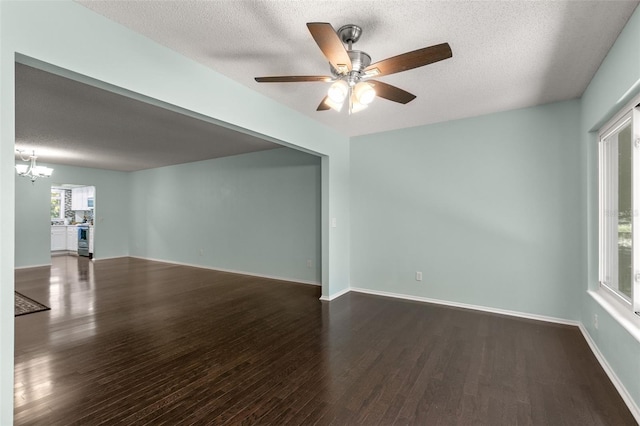 empty room with dark hardwood / wood-style flooring, ceiling fan with notable chandelier, and a textured ceiling