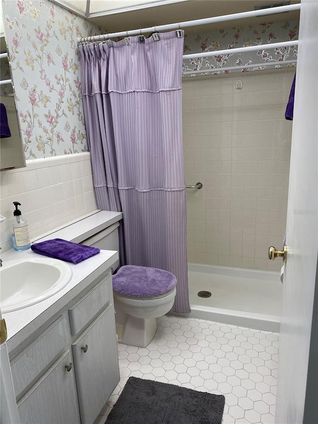 bathroom with tile walls, toilet, tile patterned floors, vanity, and curtained shower