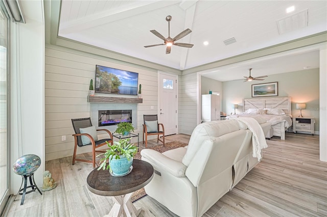 living room featuring vaulted ceiling with beams, wood walls, ceiling fan, and light hardwood / wood-style flooring