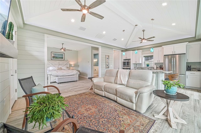 living room with vaulted ceiling with beams, light hardwood / wood-style floors, ceiling fan, and wood walls