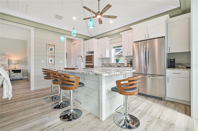 kitchen featuring light stone counters, white cabinets, stainless steel appliances, a kitchen bar, and a center island with sink