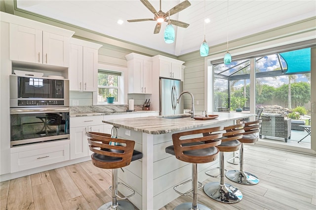 kitchen featuring white cabinets, an island with sink, appliances with stainless steel finishes, light stone countertops, and a kitchen bar