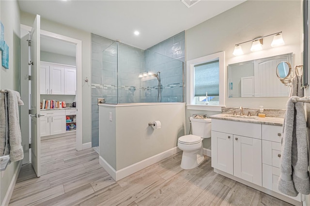 bathroom with hardwood / wood-style floors, tiled shower, vanity, and toilet