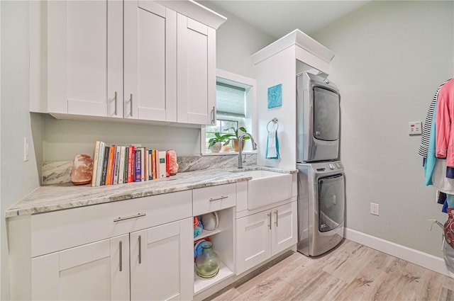 laundry area featuring stacked washer / drying machine, sink, light hardwood / wood-style flooring, and cabinets