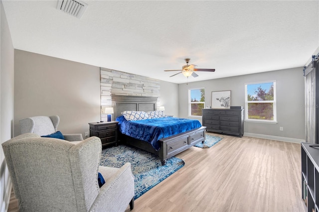 bedroom with a textured ceiling, a fireplace, ceiling fan, and light hardwood / wood-style flooring