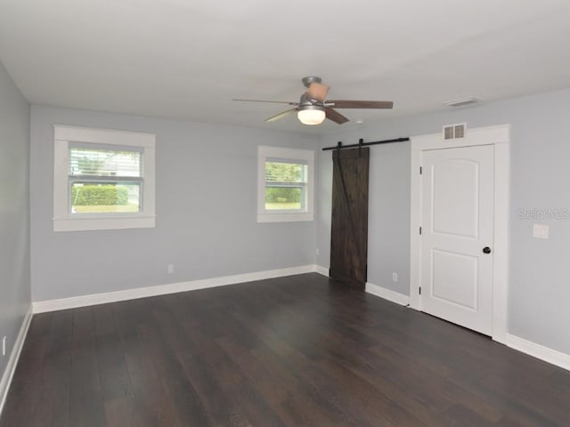 spare room featuring a wealth of natural light, ceiling fan, dark hardwood / wood-style floors, and a barn door