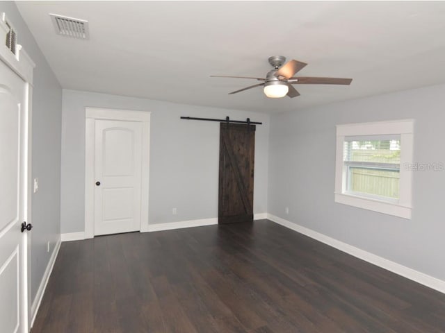 unfurnished bedroom featuring ceiling fan, dark hardwood / wood-style floors, and a barn door