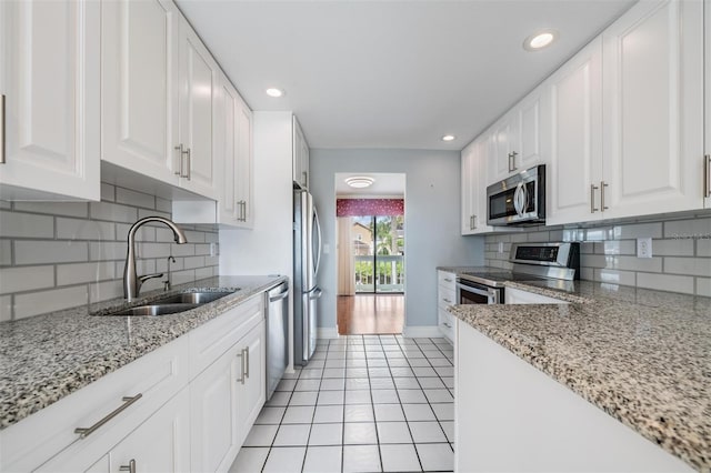 kitchen with white cabinetry, light stone counters, light tile patterned floors, stainless steel appliances, and sink