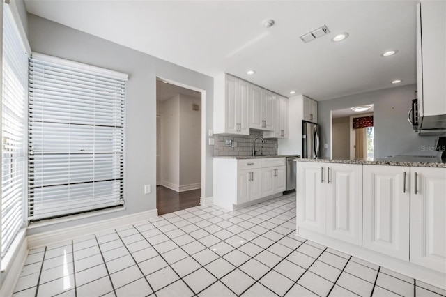 kitchen with light tile patterned floors, stainless steel appliances, light stone counters, tasteful backsplash, and white cabinets