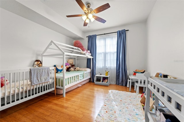 bedroom featuring ceiling fan, a nursery area, and hardwood / wood-style flooring