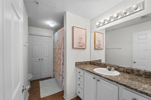 bathroom with tile patterned flooring, a textured ceiling, vanity, and toilet